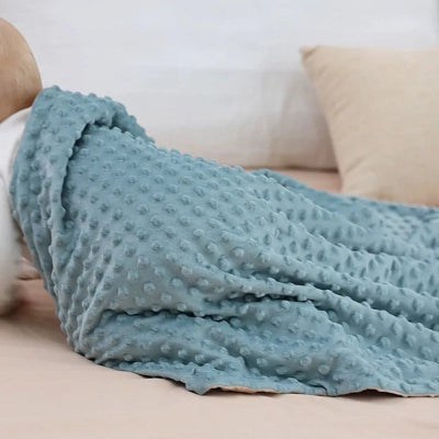 Bébé blotti dans son lit, recouvert de la couverture bebe en velours respirant vert et beige.