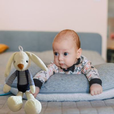 Bébé calme couché sur coussin d'allaitement regarde son son doudou lapin bunny.
