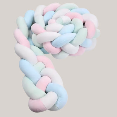 Tour de lit tressé rose, bleu, blanc et vert placé sur un fond gris doux.