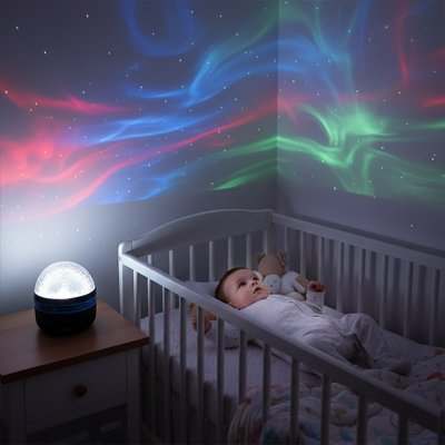 Bébé allongé dans son lit enchanté par atmosphère crée grâce à la veilleuse projection ciel étoilé magique.