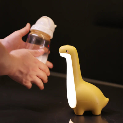 Veilleuse bébé dinosaure jaune illumine pour permettre de faire le biberon dans la nuit.