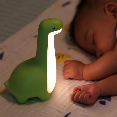Bébé dort tranquillement à côté de sa veilleuse bébé dinosaure vert.
