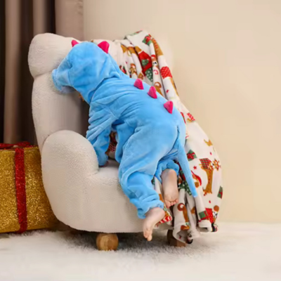 Petit garçon essaie de s'asseoir sur le sofa portant sa barboteuse câlin mignon dragon bleu.