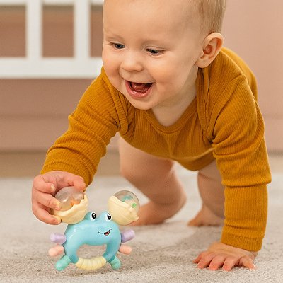 Bébé qui tente d’attraper son hochet bébé en forme de crabe avec ses petites mains.