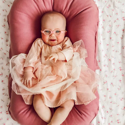 Un bébé fille souriante couchée dans son cocon bebe multifonctionnel rose.