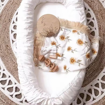 Cocon bebe blanc avec objet nouveau-né dedans déposé sur le tapis.