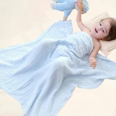 Un enfant couché dans son lit couvert avec sa couverture bébé bleu en coton.