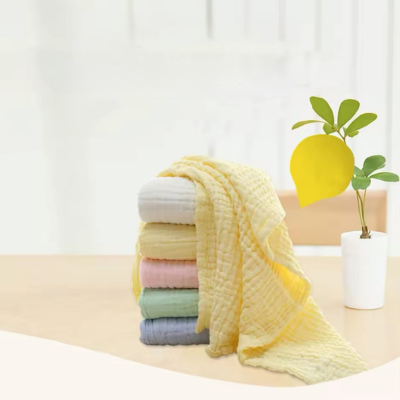 Les couvertures de différente couleur pliées et posé l'une sur l'autre et la couverture bébé en coton jaune déplié mise en avant. 