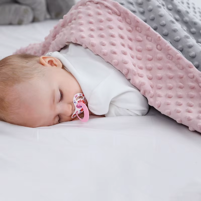 Bébé dort confortablement couvert avec la couverture en velours respirant rose et gris.