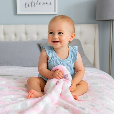 Bébé assis sur le lit touchant sa couverture bebe ultra-douce, éléphant.