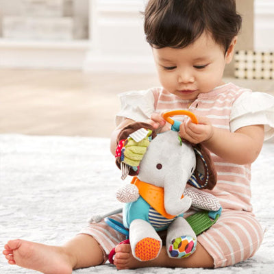 Petite fille en train de jouer avec son doudou bebe, Cozyrattle, assis sur le plancher.