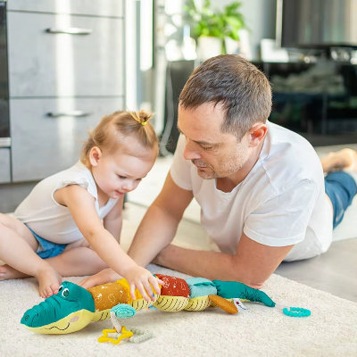 Un enfant joue avec son doudou bebe crocodile à côté de son papa.