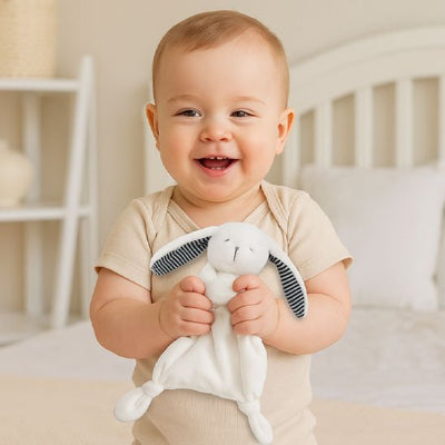 Bébé assis sur son lit souriant serre le doudou bébé dans ses mains. 