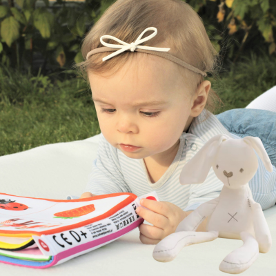 Petite fille lit dans son livre en présence de son doudou lapin apaisant.
