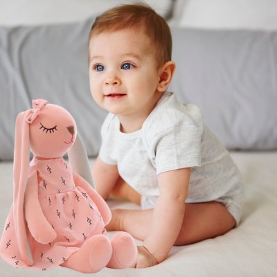 Bébé assis sur son lit à côté de son doudou lapin Lili enchanteur.