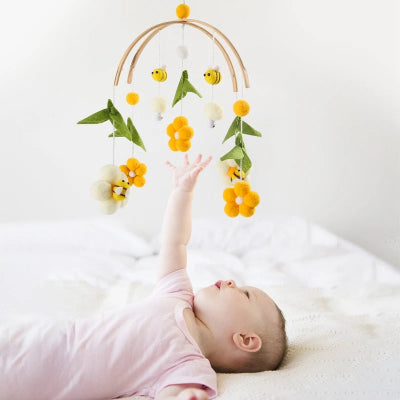 un bébé couché dans son berceau essaye d'attraper les fleurs suspendus sur le mobile bébé.