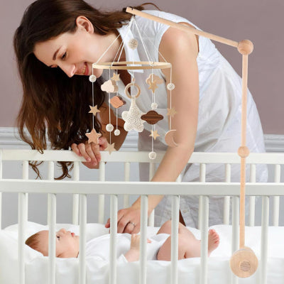 une maman souriante regarde sur son lit de bébé qui est jouit par ce mobile bebe.