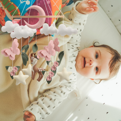 Mobile bébé papillons suspendu sur le lit d'une petite fille qui joue avec lui.