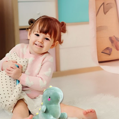 Petite fille joue avec sa peluche T-Rex, placé devant elle.