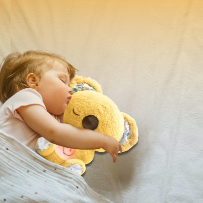Bébé dort avec sa peluche koala jaune dans ses bras.