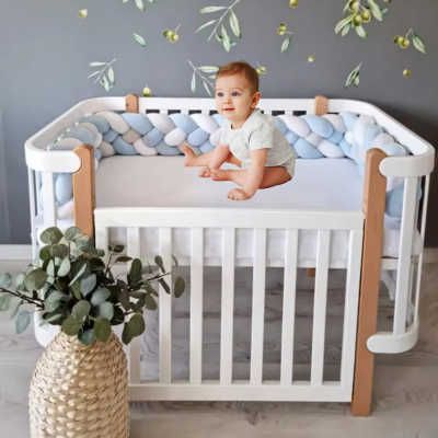 Tour de lit bebe bleu, blanc et gris 3 brins, installé sur le lit de bébé, assis sur celui-ci.