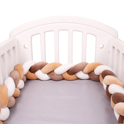 le tour de lit tressé beige brun et blanc fait le périmètre de lit à barreaux.