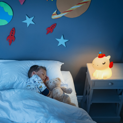 Veilleuse bébé Licorne éclairant légèrement la chambre pendant que le bébé dort à proximité.
