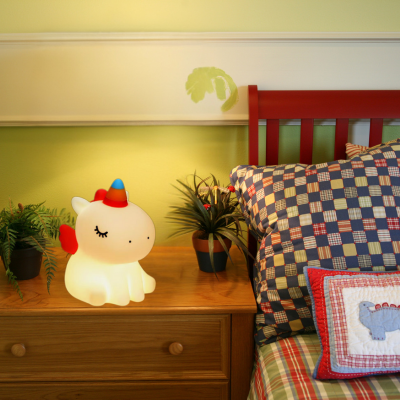 Veilleuse bébé licorne déposée sur la table de chevet près du lit de l'enfant.