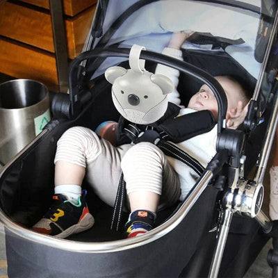 Veilleuse bruit blanc koala suspendu sur une poussette. L'enfant est couché dedans.