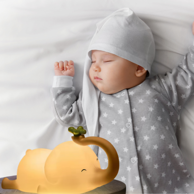 Bébé dort paisiblement à côté de la veilleuse enfant éléphant relaxante.